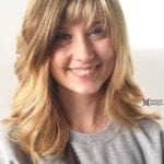 Smiling young woman with blonde hair and bangs in a gray shirt.