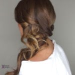 A woman with long brown hair styled in loose curls and a partial braid.