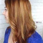 Profile view of a woman with layered, highlighted auburn hair.