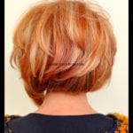 Back view of a woman with a short, layered haircut dyed in shades of blonde and light brown.