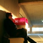 A person sitting alone in a dimly lit parking garage with a sunset glow.