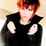 A person with red hair and a black coat posing.