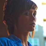 A woman with short hair looks sideways in soft lighting.