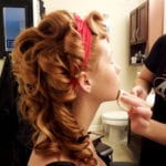 A woman having makeup applied with a red headband in her hair.
