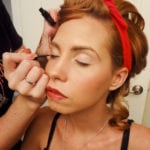 A woman having eyeshadow applied by a makeup artist.