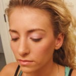 A close-up of a woman with closed eyes and curly blonde hair.
