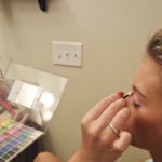 A person applying makeup with a brush in front of a mirror.