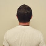 Back view of a man wearing a white shirt against a plain wall.