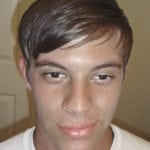 Close-up portrait of a young man with brown hair and a neutral expression.