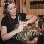 A woman styling another woman's braided hair indoors.