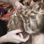 Hands braiding blonde hair into a detailed style.