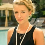 Young woman with braided hair and layered necklaces by a pool.