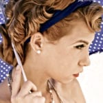 A woman holding a stick, wearing a blue headband and pearl earrings.