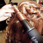 A person curling brown hair with a curling iron.