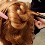 A close-up of a person styling blonde hair into an intricate updo.