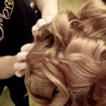 A close-up of hands styling thick, wavy blonde hair.