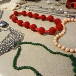 Various beaded necklaces in red, green, pink, and silver colors.