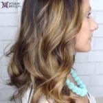 Side profile of a woman with wavy blonde and brown balayage hair wearing a turquoise necklace.