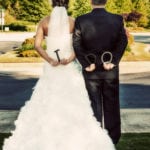 Bride and groom holding handcuffs behind their backs.
