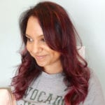 A woman with long, wavy red hair smiling gently.