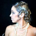 Profile of a woman with curly hair and layered pearl necklaces.