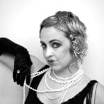 Vintage black and white portrait of a glamorous woman with curled hair and pearls.