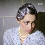 A woman with styled gray hair and pearl necklace looking down.