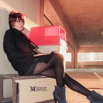 A woman sitting on a box in a parking garage wearing black outfit and boots.