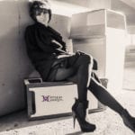 Black and white photo of a woman sitting on a box in stylish boots.