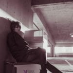 A person sitting against a wall in a dimly lit parking garage.
