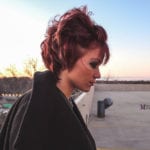 Profile of a woman with short red hair outdoors at sunset.