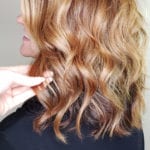 Hand touching wavy, highlighted brown hair.