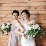 Two women in elegant dresses holding bouquets, smiling.