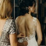 Bride in a lace wedding dress with an open back being assisted.