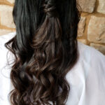 Back view of long, wavy dark hair styled half up against a stone wall.