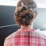 Elegant updo hairstyle with floral accessories on a woman wearing a pink plaid shirt.