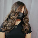 Woman with long wavy hair wearing a black mask and black shirt.