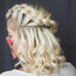 Blonde curly hair styled with a braided crown on a dark background.